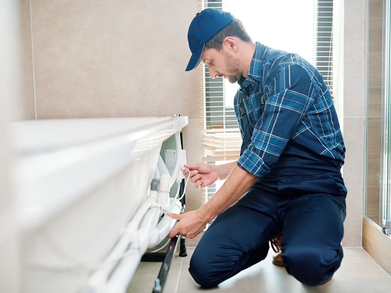 Contemporary technician of household maintenance service in workwear installing pipe system by bathtub. REPAIRING FAUCET, TOILET, AND BATHTUB LEAKS IN GLENVIEW IL WITH JPW PLUMBING, leak repair